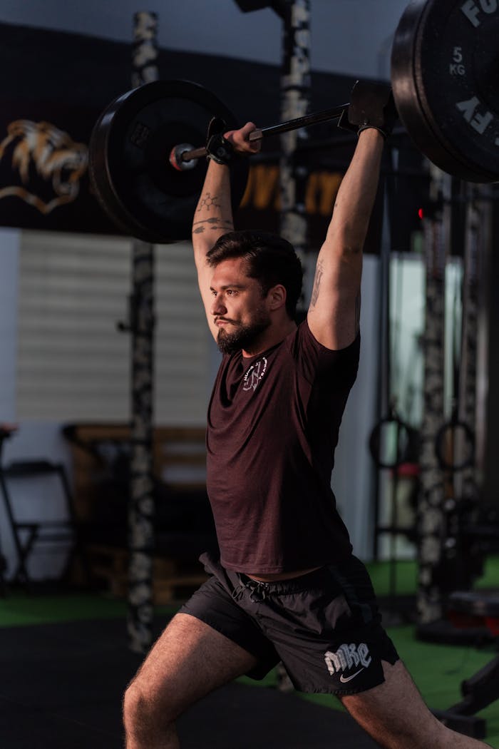 Adult male performing weightlifting exercise in a gym, focused on fitness and strength.